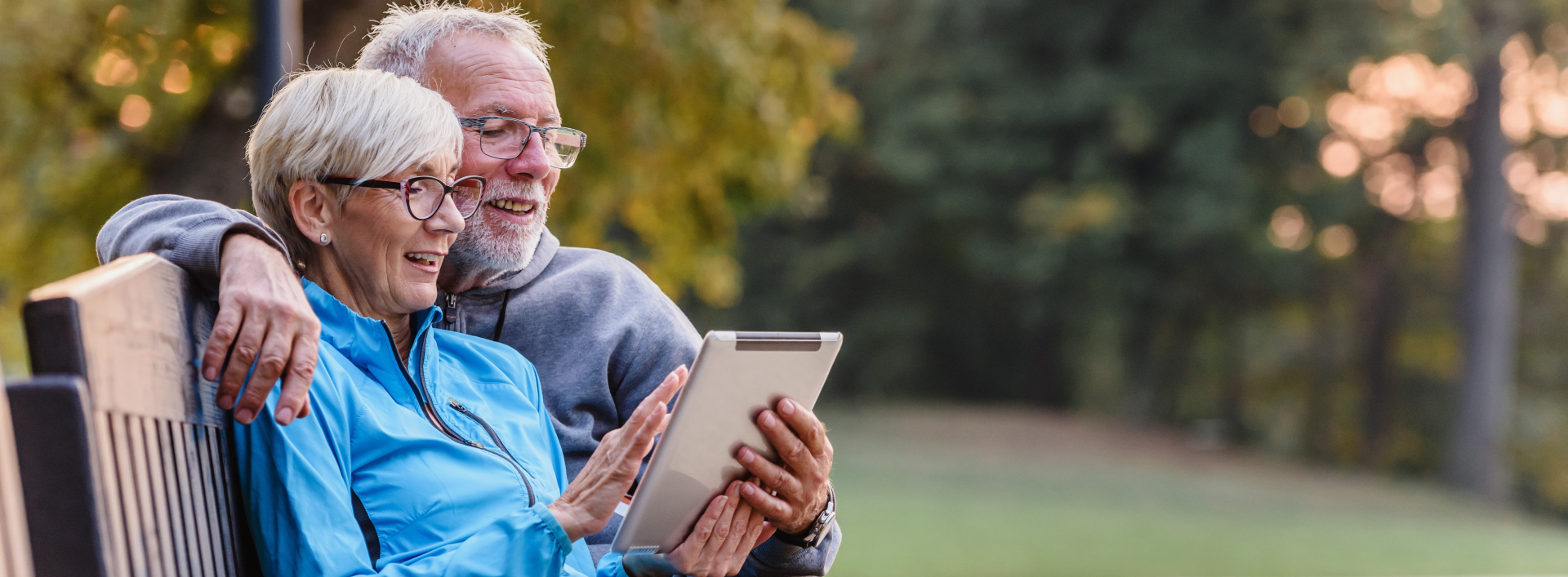 Male-presenting and female-presenting older individuals looking at tablet device